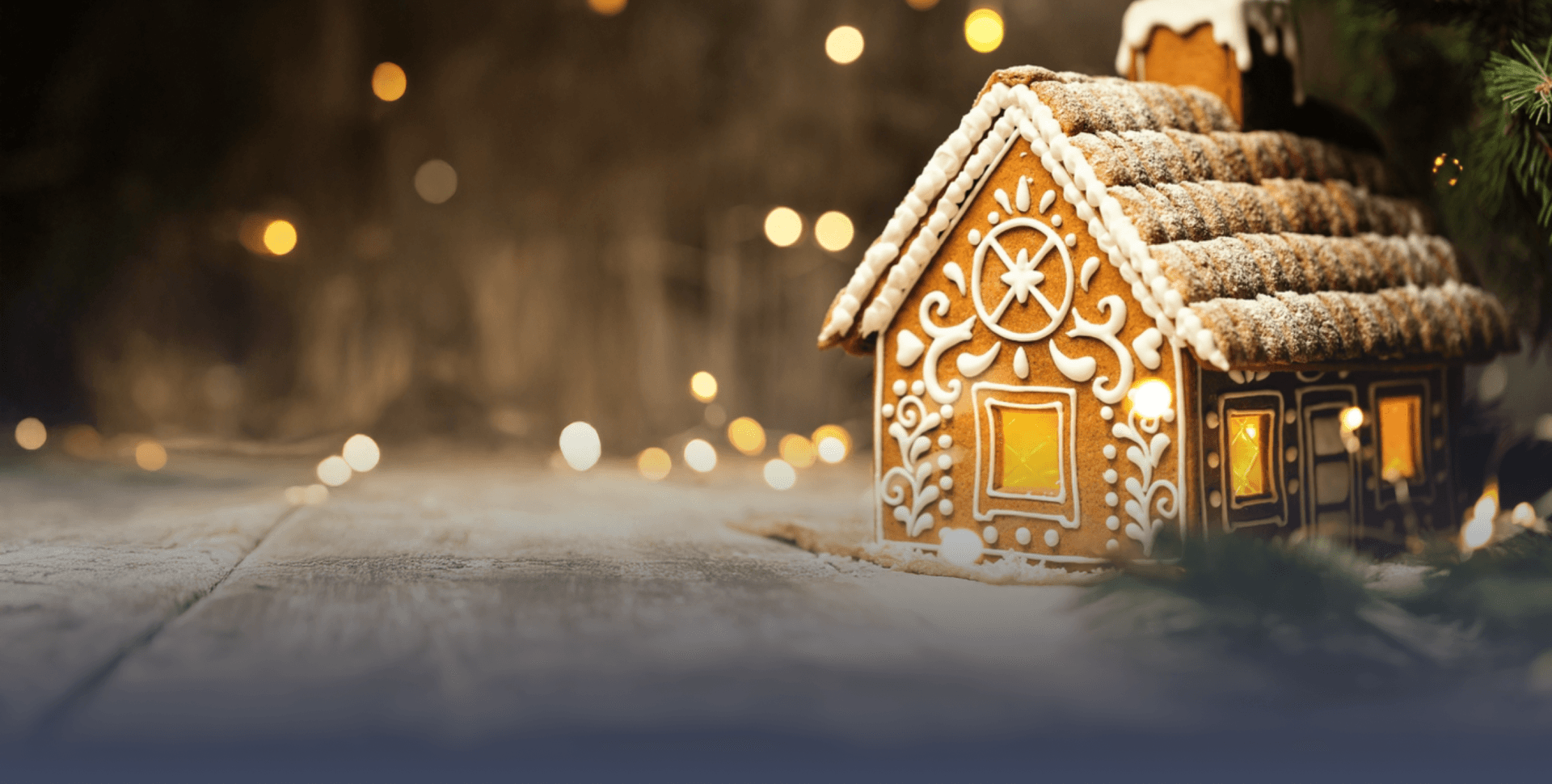 Gingerbread house surrounded by fairy lights with a Christmas tree in the background