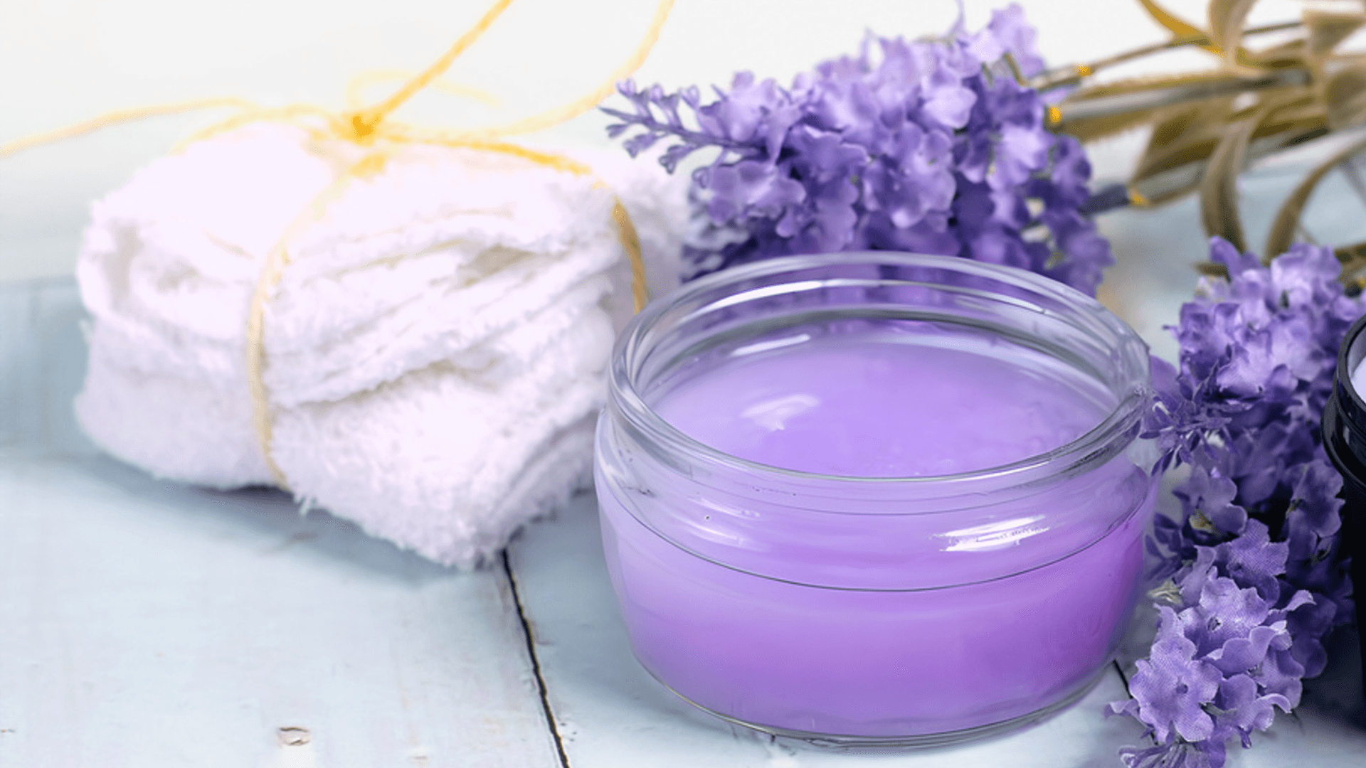 Pot of purple balm surrounded by flowers and a towel