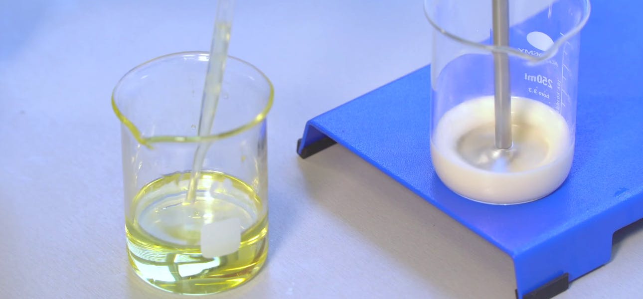 1 beaker with yellow oil and a pipette, next to a beaker on a mixer with a white liquid in it